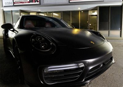 Satin black Porsche 911 Turbo parked in front of the San Diego storefront