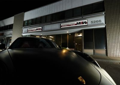 Satin black Porsche 911 Turbo parked outside the San Diego shop storefront