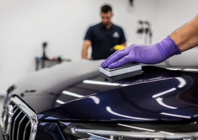 Technician applying ceramic coating to a dark blue car hood in San Diego