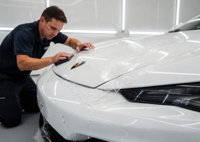 Installer smoothing XPEL paint protection film onto a white car hood